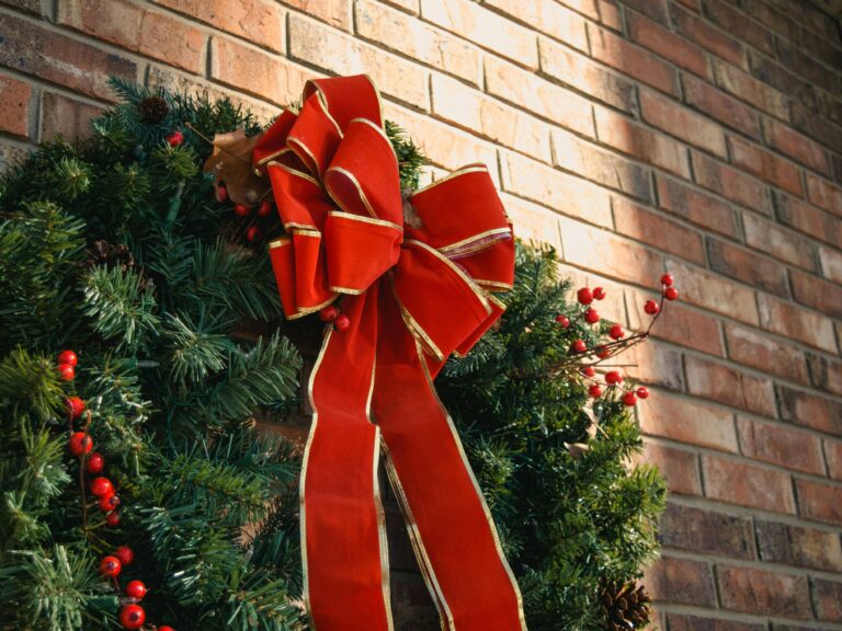 Close-up of a traditional Christmas wreath with a red bow hanging on a brick wall, capturing the holiday spirit.